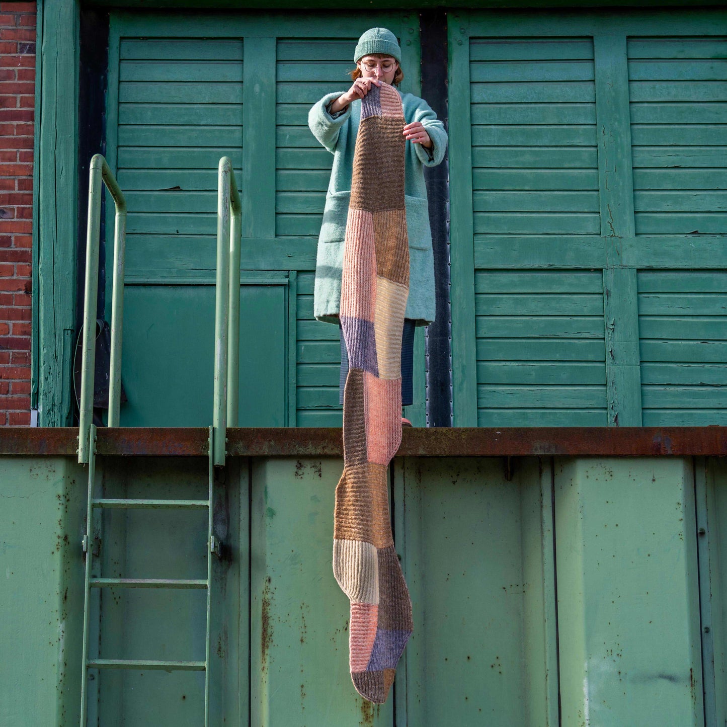 Anna Husemann holding her Forming Scarf in the air in a green harbour surrounding.