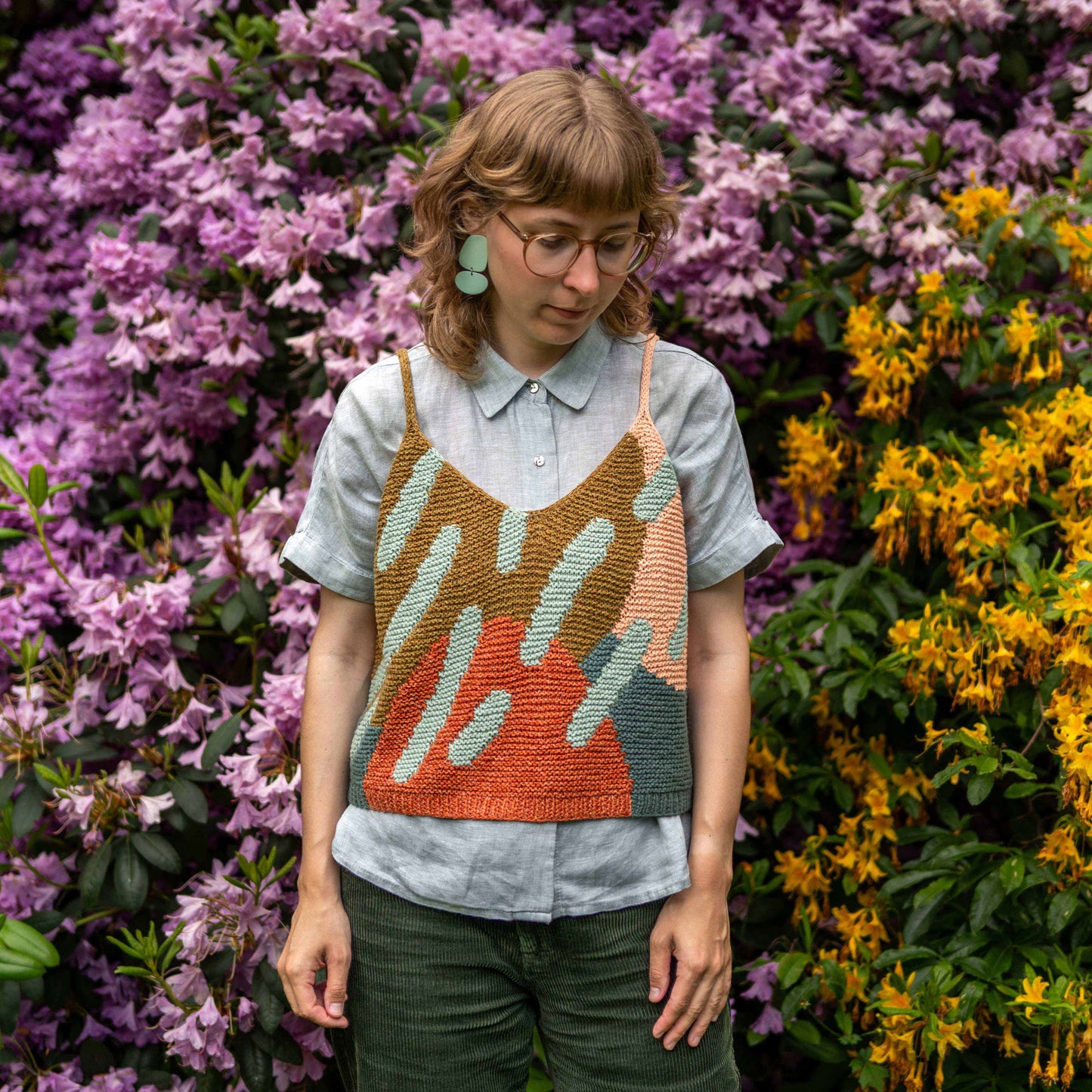 Anna Husemann wearing her colourful Intarsia Top in front of lots of flowers.