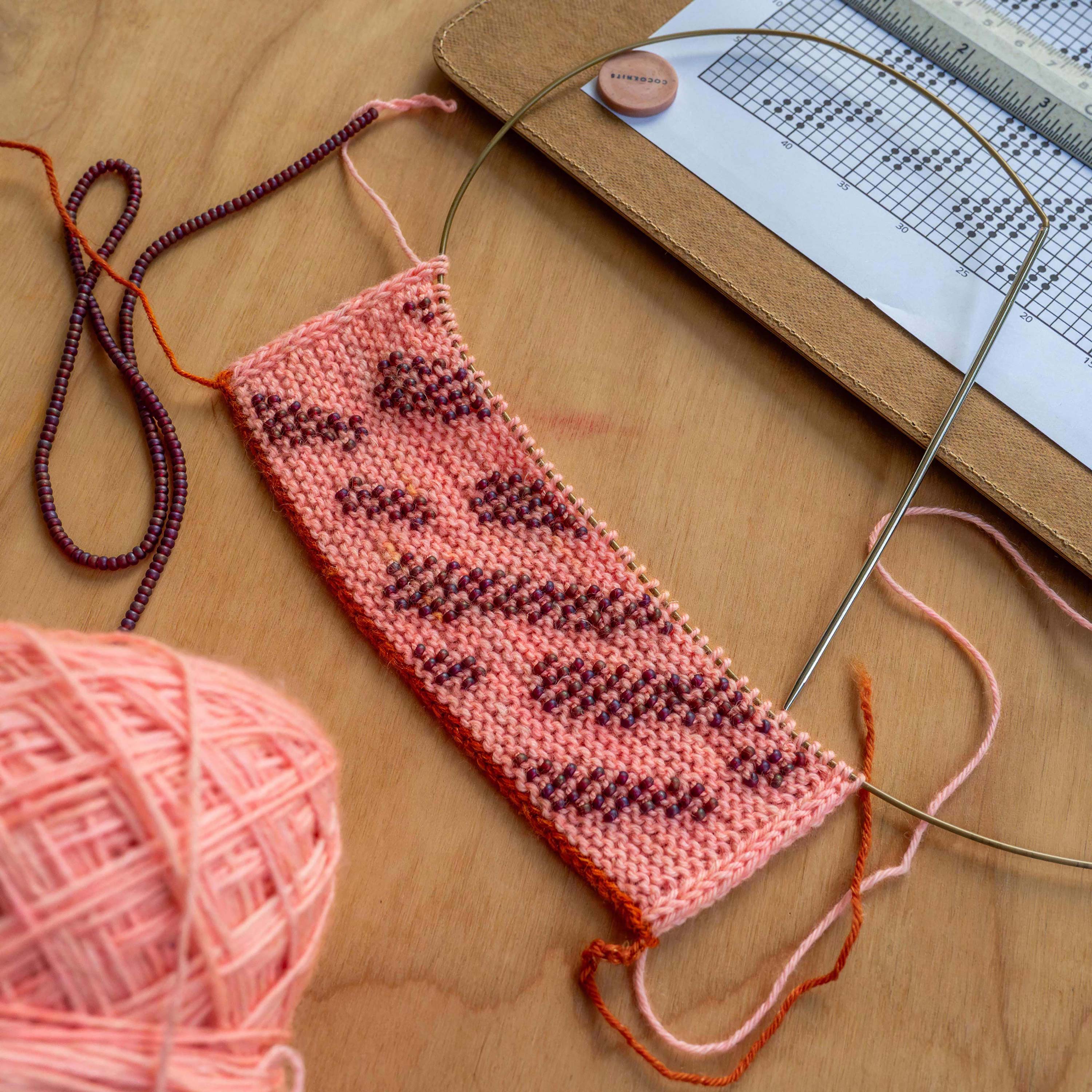 Knit swatch with beads laying on a table next to a knit chart.