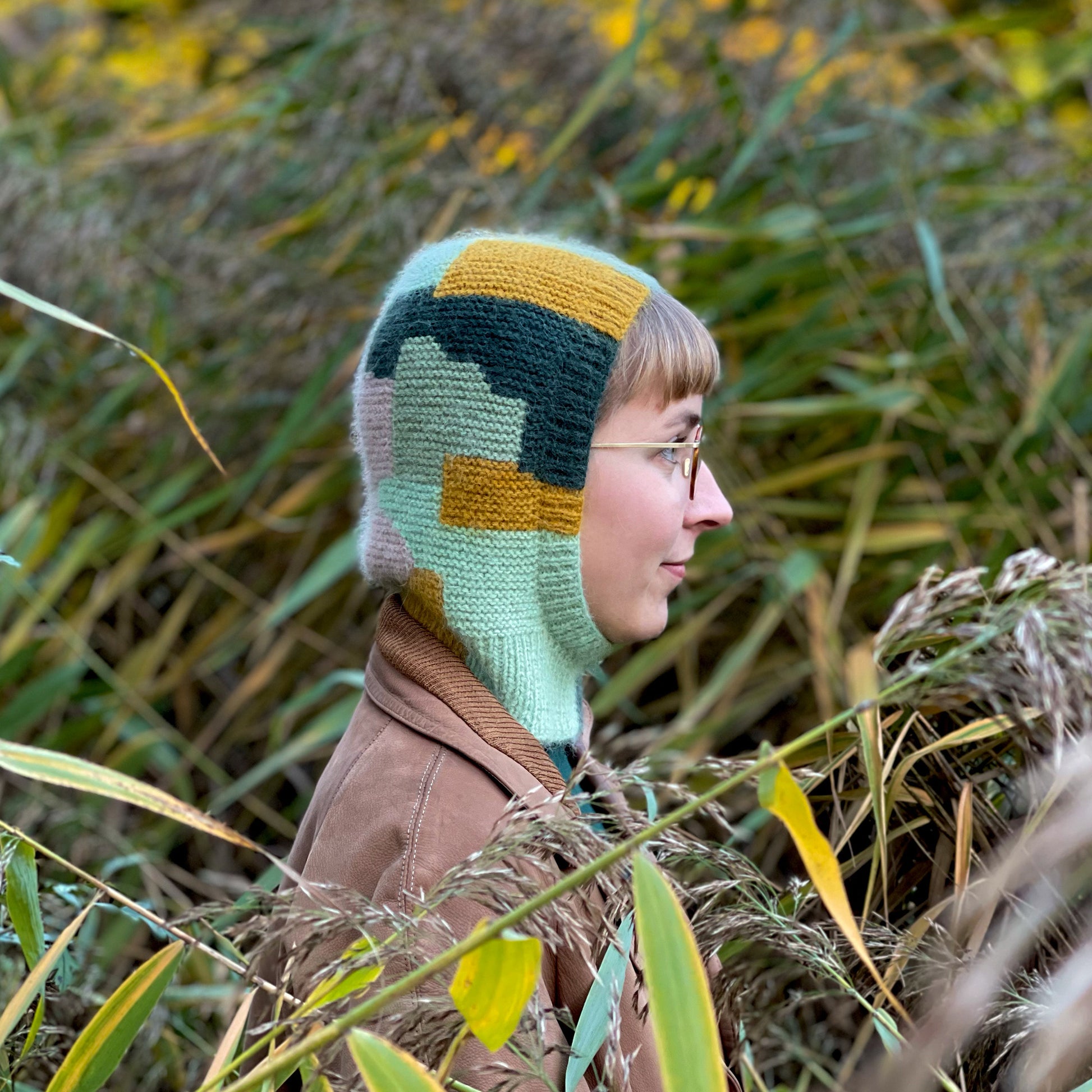 Anna Husemann wearing her Intarsia Balaclava in a green, leafy spot.