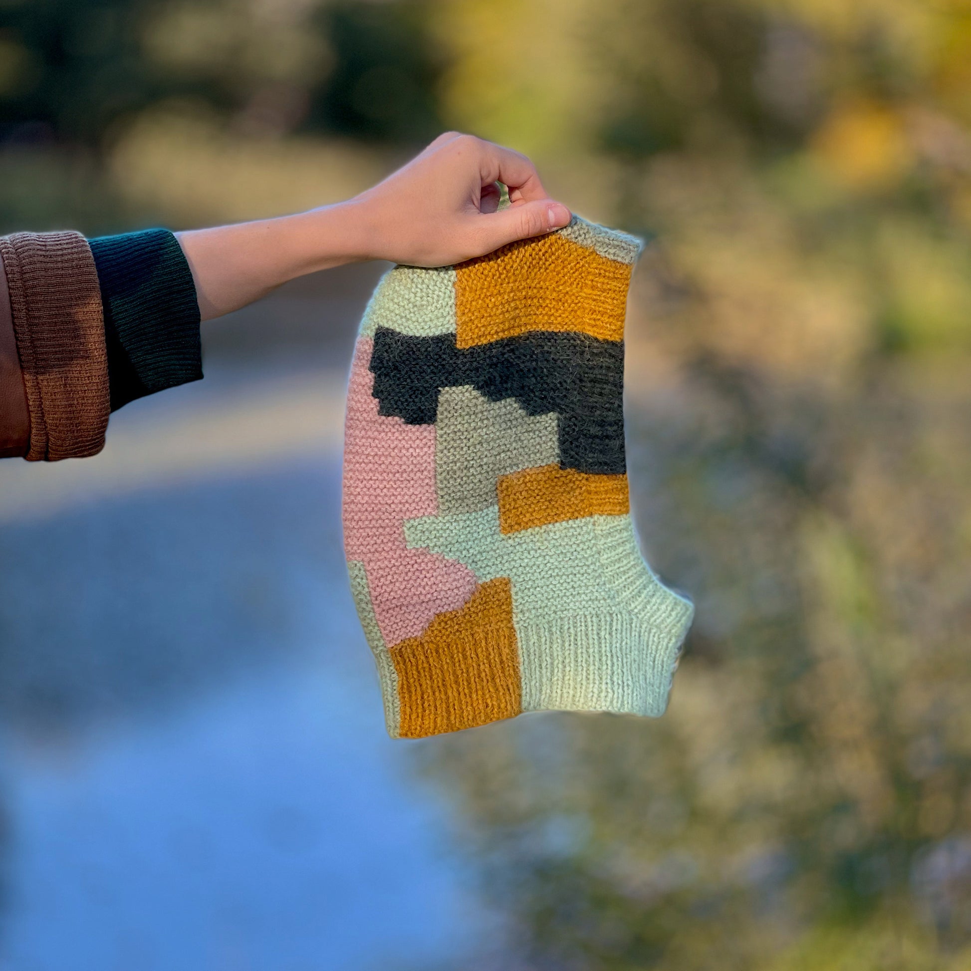 Anna Husemann holding her Intarsia Balaclava in front of a blurry autmunal background.